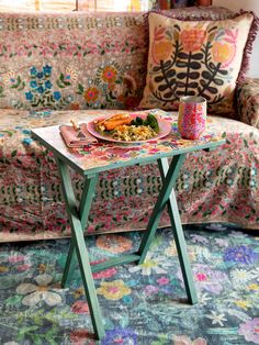 a table that has food on it in front of a couch with pillows and flowers