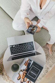 a woman sitting on a couch with a laptop and magazine in front of her feet