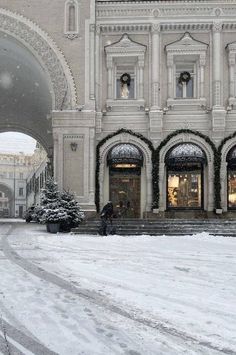 people are walking through the snow in front of a large building with arched doorways