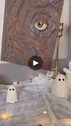 two white ghost figurines sitting on top of a bed next to a painting