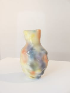 a multicolored vase sitting on top of a white table next to a wall