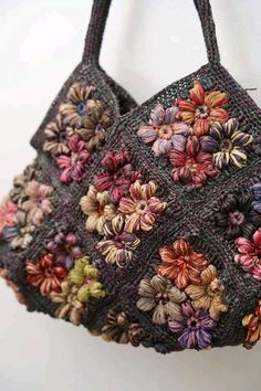 a crocheted purse with flowers on it hanging from a hook in front of a white wall