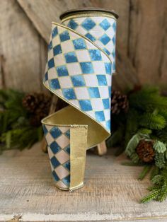 a blue and white checkerboard design canister with gold trim on it next to pine cones