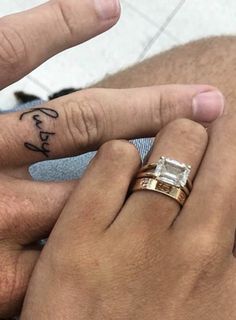 two people holding hands with tattoos on their fingers and one has a small diamond ring