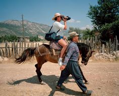 a man riding on the back of a brown horse while holding onto a woman's purse