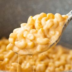 a spoon full of macaroni and cheese being lifted from a skillet with it