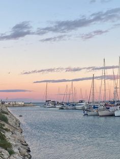 sailboats are docked in the water at dusk near a beach with rocks and grass