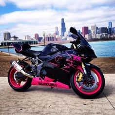 a pink and black motorcycle parked in front of a body of water with a city skyline behind it