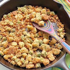 a frying pan filled with fried food on top of a colorful table cloth next to a wooden spoon