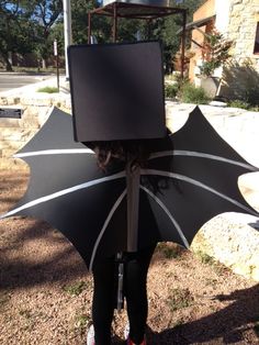 a woman standing in the grass with an umbrella shaped like a box on her head