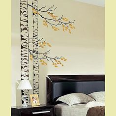 a bed room with a neatly made bed and a tree decal on the wall