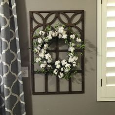 a wreath is hung on the wall next to a window with shutters and drapes