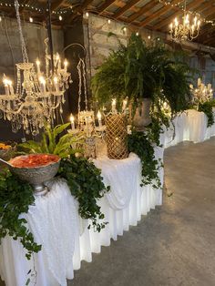 an arrangement of plants and flowers on a table with chandelier hanging from the ceiling