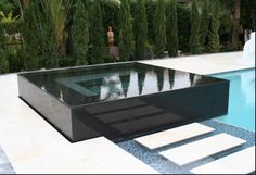 an outdoor pool surrounded by trees and water features a large rectangular glass table that sits in the center of the pool