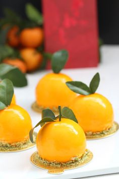 three oranges with leaves on them sitting on small gold plated coasters in front of red box