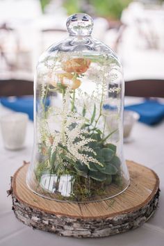 a glass clochet with flowers in it on top of a wooden slice at a table