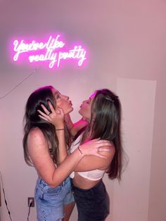 two young women hugging each other in front of a neon sign that says, you're the really party