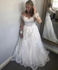 a woman standing in front of a mirror wearing a white wedding dress with sheer sleeves