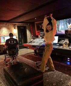 a woman standing in front of a mixing desk with headphones on and arms up