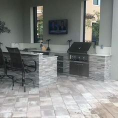 an outdoor kitchen with grill, sink and chairs