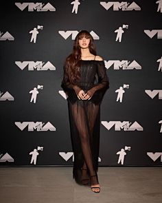 a woman standing in front of a wall wearing a sheer black dress with long sleeves