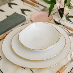 the table is set with white and gold plates, silverware, and pink flowers