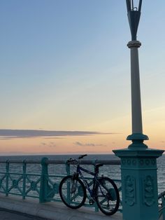 a bike parked on the side of a bridge near the ocean at sunset or dawn