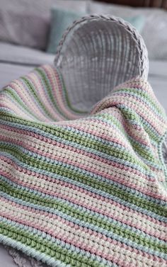 a crocheted blanket sitting on top of a bed next to a metal basket