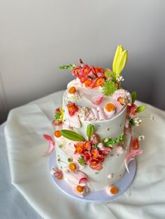 a three tiered cake with flowers and leaves on the top is sitting on a white table cloth