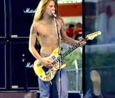 a shirtless man holding a guitar and singing into a microphone