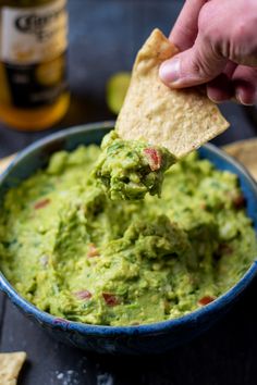 a person dipping guacamole into a blue bowl with tortilla chips