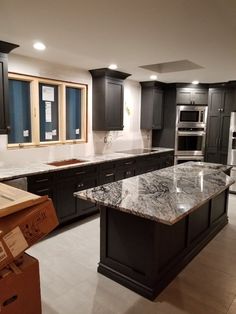 a large kitchen with black cabinets and marble counter tops, an island in the middle