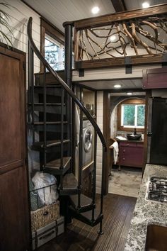 a spiral staircase in a tiny home with wood floors and white walls, leading to the kitchen