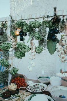 an assortment of vegetables are hanging from the ceiling in front of a table with plates and bowls on it