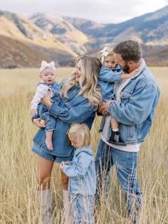 a man and woman holding their two children in a field with mountains in the background