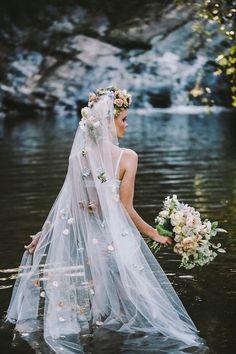 a woman in a wedding dress standing in the water with her veil over her head