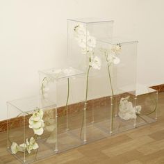 three clear vases with flowers in them sitting on the floor next to each other