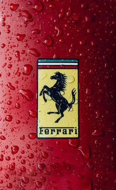 the ferrari logo is shown on a red car with water droplets around it and there are other cars in the background