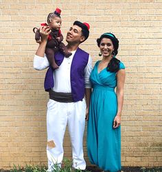 a man and woman are standing in front of a brick wall with a baby on his shoulders