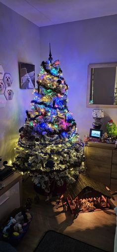 a brightly lit christmas tree in the corner of a room with other items on the floor