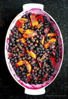 a bowl filled with blueberries and peaches on top of a black countertop