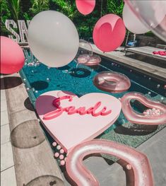 balloons floating in the air next to a pool filled with pink and white letters that spell love