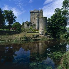 an old castle sitting on top of a lush green hillside next to a small river