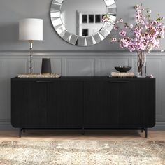 a living room with a large mirror on the wall and a black sideboard in front of it