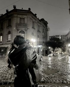 black and white photograph of a woman walking down the street in the rain at night