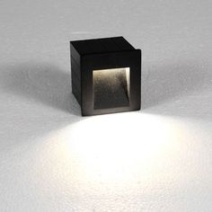 a small square object is lit up on the floor with light coming from behind it