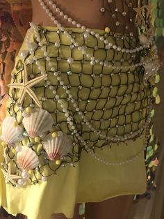 a close up of a person wearing a skirt with shells on it and pearls around the waist