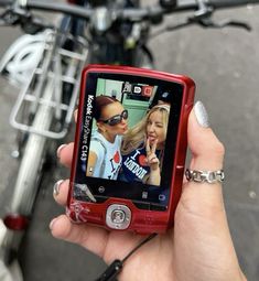 a woman holding up a red cell phone to take a picture with her friend on the screen