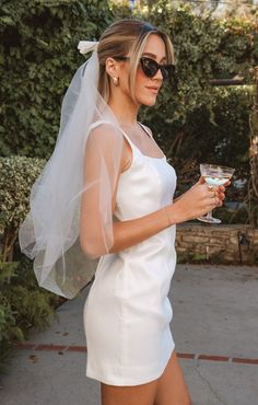 a woman in a white dress holding a wine glass and wearing a veil over her head