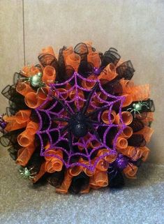 an orange and purple wreath with spider webs on it sitting on the floor next to a wall